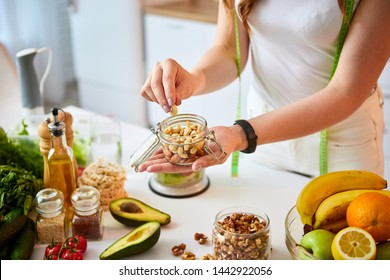 Young Happy Woman Eating Different Nuts (cashew, Hazelnut, Almond) In Modern Kitchen. Healthy Food And Dieting Concept. Loosing Weight