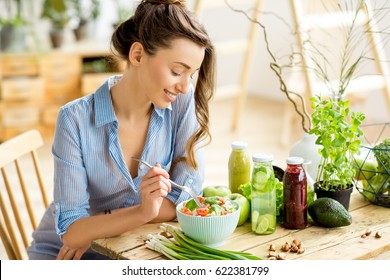 Young and happy woman eating healthy salad sitting on the table with green fresh ingredients indoors - Shutterstock ID 622381799