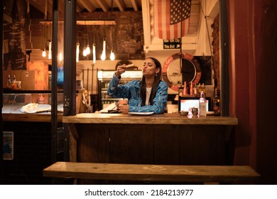 A Young And Happy Woman Eating Pizza Sitting Alone In An Empty And Dark American Restaurant. A Female Relaxing And Enjoying Delicious Food Late At Night In A Cosy Junk Food, Takeaway Cafe