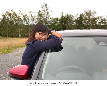 A Young Happy Woman Embracing Her Favourite Red Car In A Grass Field