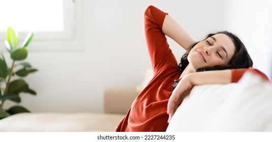 Young happy woman feeling comfortable and relaxed leaning head on her couch at home with eyes closed - Shutterstock ID 2227244235