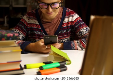 Young Happy Woman In Glasses Study At Night. Millennial Student Scrolling Phone. Blurred Books And Markers On Foreground. Education And Learning Concept. Online.