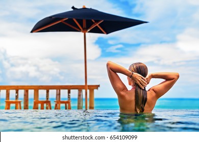 Young happy woman have fun in outdoor infinity pool with view to ocean surf. Positive girl swim, relax at poolside. Healthy lifestyle, people on family summer beach holiday. - Powered by Shutterstock