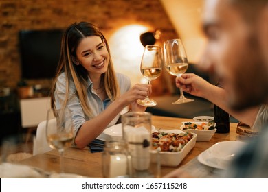 Young Happy Woman And Her Friends Toasting With Wine While Eating Dinner In Dining Room.