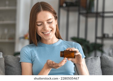 Young happy woman holding a bottle of pills capsules takes daily medication, supplements, vitamins to strengthen hair nails or hair, smiling friendly, health care concept - Powered by Shutterstock