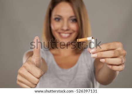 young happy woman holding a broken cigarette and showing thumbs up