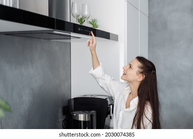 Young happy woman housewife using black cooking exhaust with touch screen on control panel above electric stove while preparing in minimalistic fully furnished kitchen with integrated appliances - Shutterstock ID 2030074385