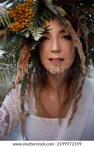 A young happy woman in a large wreath of ears and field grasses, folk-style costume, close-up