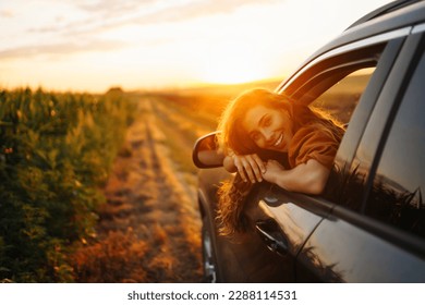 Young happy woman leaning out of the car window enjoying the sunset. The concept of active lifestyle, travel, tourism, nature. - Powered by Shutterstock