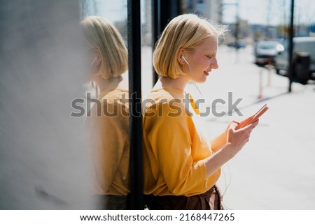 Young happy woman listening music outdoors. Positive blonde girl with headphones enjoying in sunny day