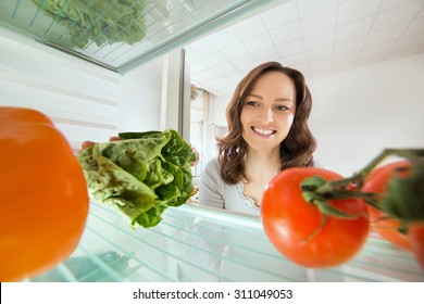 Young Happy Woman Looking At Vegetables View From Inside Fridge