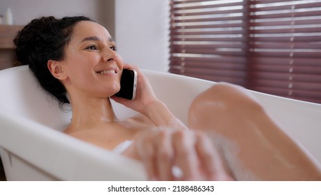 Young happy woman lying in foam comfort bath bathing relaxing in bathroom talking on mobile phone laughing answering friendly call enjoys pleasant conversation using smartphone hygienic daily - Powered by Shutterstock