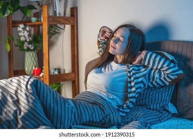 A Young Happy Woman Is Lying In Her Cozy Bed, Stretching And Getting Ready For Bed. Concept Of Bedtime Pastime And Rituals For A Healthy And Restful Sleep.