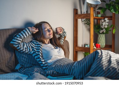 A Young Happy Woman Is Lying In Her Cozy Bed, Stretching And Getting Ready For Bed. Concept Of Bedtime Pastime And Rituals For A Healthy And Restful Sleep.