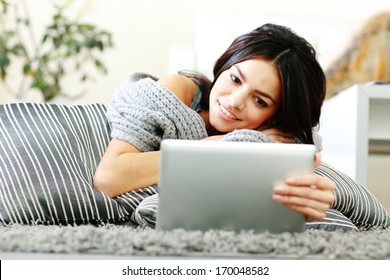 Young Happy Woman Lying On The Floor With Pillows And Using Tablet Computer At Home