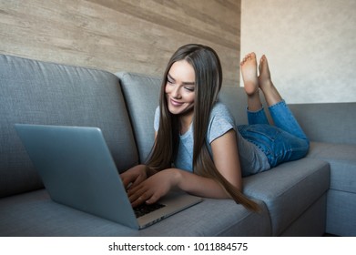 Young happy woman lying relaxed on belly on sofa with  laptop 