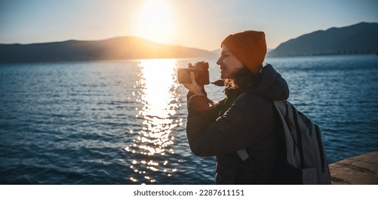 Young happy woman photographer and traveler standing with photo camera on the seashore at sunset - Powered by Shutterstock