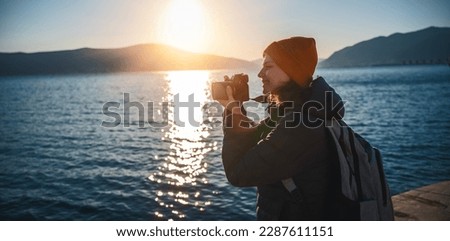 Young happy woman photographer and traveler standing with photo camera on the seashore at sunset