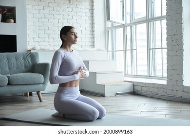 Young happy woman practicing yoga and doing breathing exercises and meditating. Female enjoying fitness pilates workout alone at home. Healthy and balanced lifestyle.