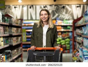 young happy woman pushing trolley spends time in a supermarket or mall store. Female walk with a cart. Daily Shopping and grocery Items Food In Market. joyful Pretty woman in casual clothes walking - Powered by Shutterstock