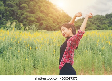 Young happy woman raising hands in yellow flower field on sunset,mountain view backgound.