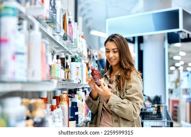 Young happy woman reading ingredients of skin care product while shopping at the store. - Shutterstock ID 2259599315
