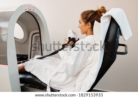 Young happy woman receiving oxygen therapy in hyperbaric chamber at health spa.