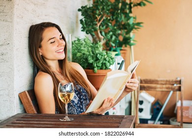 Young Happy Woman Relaxing On The Balcony, Reading Book, Leaning On The Wall, Drinking Glass Of Wine