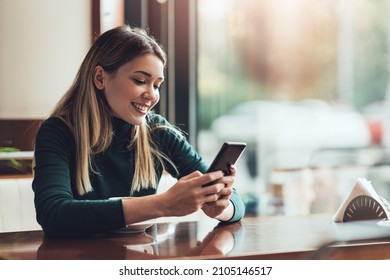 Young happy woman at restaurant drinking coffee and using mobile phone. - Powered by Shutterstock