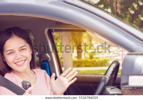 Young\
happy woman shows car key out of window. Attractive Asian female\
happy taking car key from dealer in auto show or salon. Auto\
business, car sale, consumerism and people\
concept,