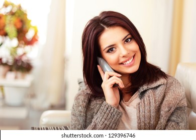 Young Happy Woman Sitting On The Sofa At Home While Talking On Phone