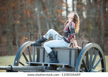 Young happy woman sitting on old cannon carriage in Manassas National Battlefield Park in Virginia where Bull Run battle was fought, sunlight