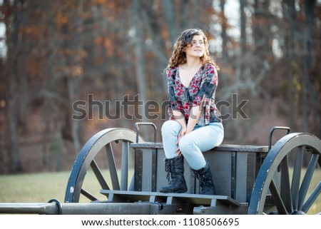 Young happy woman smiling sitting on old cannon carriage in Manassas National Battlefield Park in Virginia where Bull Run battle was fought, sunlight