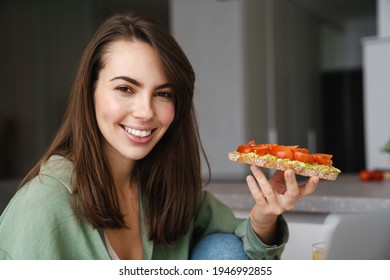 Young Happy Woman Smiling While Eating Avocado Toast At Home Kitchen