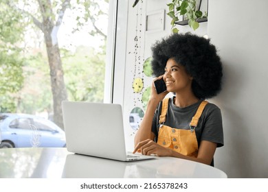 Young Happy Woman Speaking On Phone Using Laptop In Cafe.