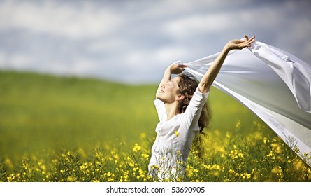 Young happy woman standing in yellow rapeseed field holding a white piece of cloth in the wind expressing freedom. - Powered by Shutterstock