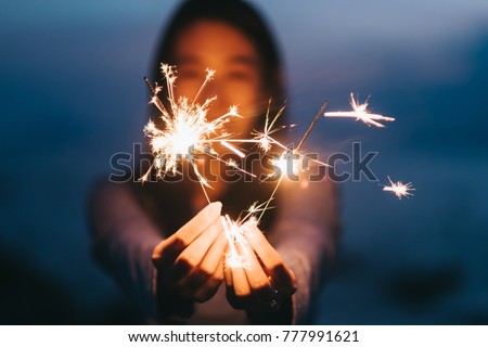 Young happy woman stands on beach with sparkler in sunset light.
