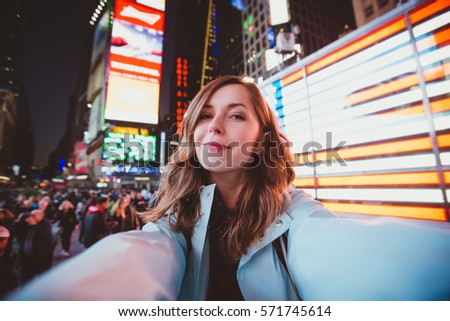 Young happy woman taking selfie on Times Square at night, Manhattan. Inspiring New York atmosphere and a beautiful smiling girl.