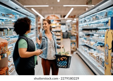 Young happy woman talking to female worker while buying dairy products at supermarket. - Powered by Shutterstock