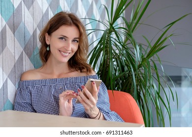 Young Happy Woman Talking On Mobile Phone With Friend While Sitting Alone In Modern Coffee Shop Interior, Smiling Hipster Girl Calling With Cell Telephone While Relaxing After Walking In Summer Day