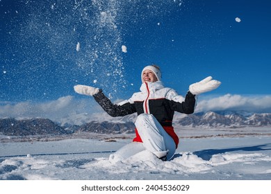 Young happy woman throw snow on winter mountains background