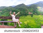 Young happy woman tourist enjoying and relaxing with beautiful landscape view rice paddy field while traveling at Nan, Thailand