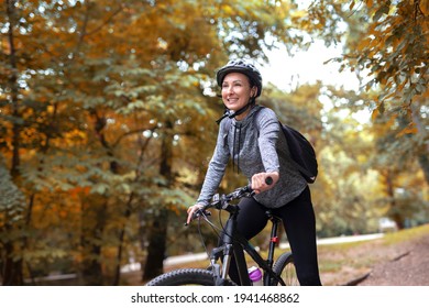 Young and happy woman in a tracksuit on a mountain bike enjoys in day ride through the park