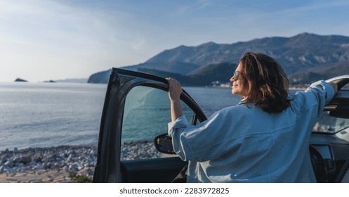 Young happy woman traveler enjoying the sunset at the sea while standing next to the car. Summer holidays and travel concept - Shutterstock ID 2283972825