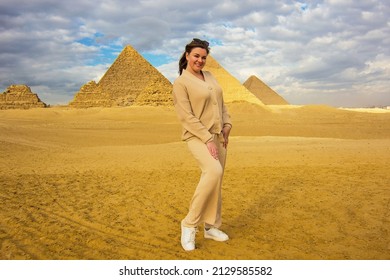 Young happy woman traveler in front of the  Great Pyramids of Giza in the desert (three small Pyramids of Queens; next in order from the left: the Pyramid of Menkaure, Khafre and Khufu), Cairo, Egypt