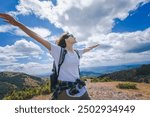 Young happy woman traveler hiker standing with outstretched arms against mountain summer landscape on top