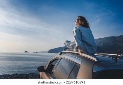 Young happy woman traveler sitting on car roof enjoying sea and sunset view. Summer vacation and adventure concept - Powered by Shutterstock