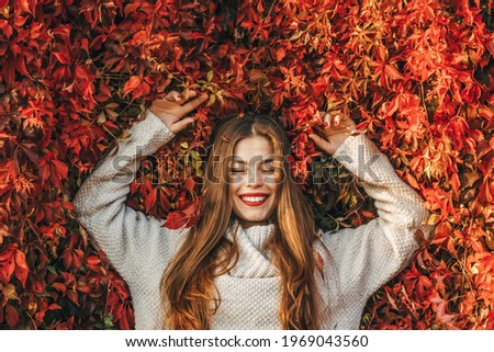 Young happy woman upon a wall of red ivy leaves.