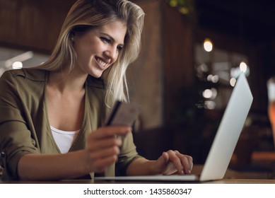 Young happy woman using credit card for online shopping in a cafe