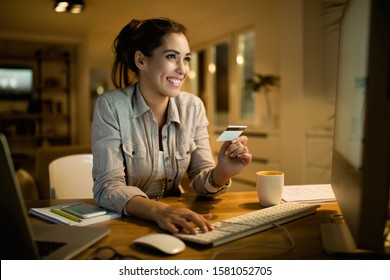 Young Happy Woman Using Credit Card For Online Shopping In The Evening At Home. 